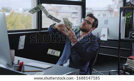 Successful young entrepreneur making money rain on a payday. Happy confident office employer celebrating financial success throwing dollars at working space.
