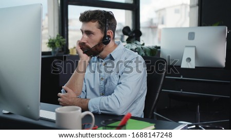 Bored young customer service executive talking with client on consulting phone call getting tired or unmotivated working by computer in the office.