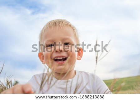 Happy little boy out doors in grass field playing smiling and handing fun.