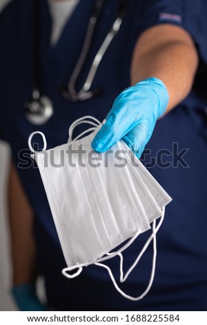 Female Doctor or Nurse Wearing Surgical Gloves Holding A Few Medical Face Masks. Royalty-Free Stock Photo #1688225584