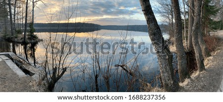 The coast at sunset, the picturesque sunset, quiet water, trees, clouds are illuminated by the sunset sun, Specular reflection in water