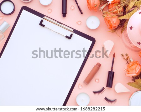 Clipboard and makeup tools and cosmetic products around it isolated on a pink peach color background. Flat lay, top view copy space. Feminine beauty blogger workplace concept.