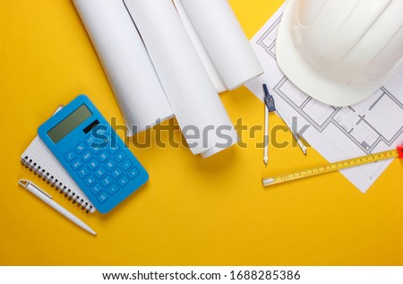 Engineering construction safety helmet, blueprint rolls, project plan and calculator on yellow background. Calculation of the cost building a house. Top view. Flat lay