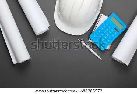 Engineering construction safety helmet, blueprint rolls, project plan and calculator on gray background. Calculation of the cost building a house. Top view. Flat lay