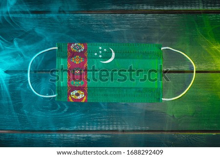Medical mask for protection against airborne diseases, painted in the national flag of Turkmenistan on a black background in blue-green smoke. Medical protection against airborne diseases, coronavirus