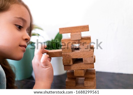 Cute girl is building a tower out of wooden blocks. Development fine motor skills in children. Child knows how to think and reason logically. Closeup of player kid. Royalty-Free Stock Photo #1688299561