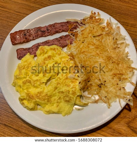 White plate with scrambled eggs, turkey bacon and hash brown potatoes.