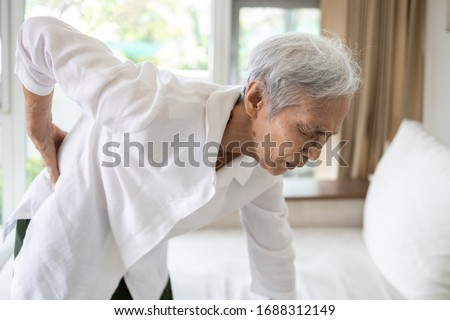Sad asian senior woman with back and hip joint painful while standing up,female patient having backache,lumbago pain,hand touch on the hip,elderly suffer from ribs hurt or waist pain,health problems Royalty-Free Stock Photo #1688312149