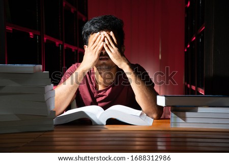 Portrait of black Thai Asian guy wear red shirt reading with stress motion looking at a lot of book in library stock photo