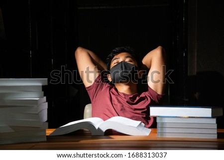 Portrait of Thai Asian black man short hair wearing mask and red shirt relax with a lot of book isolate black background stock photo