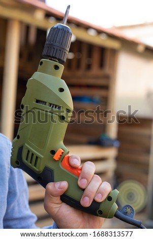 Picture of an electric drill in young man's hands, wooden background outdoor