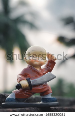 Cute sweet plastic Doll standing with sword and king costume on skateboard dress as wonder prince in action adventure. Close up portrait. Outdoor childhood fun play leisure game toddler background.