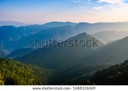 View of Himalayas mountain range with visible silhouettes through the colorful fog from Naina peak trek trail. Khalia top is at an altitude of 2615m himalayan region of Kumaon, Uttarakhand, India. Royalty-Free Stock Photo #1688326069