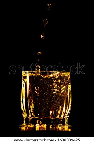 Splashes and drops of golden water in a glass are isolated on a black background.