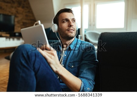Smiling man  wearing headphones and using touchpad and while relaxing in the living room.