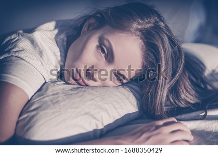 Insomnia late at night dark depressed tired young Asian woman lying on pillow bed sleepless with funny facial expression unhappy sad face. Royalty-Free Stock Photo #1688350429