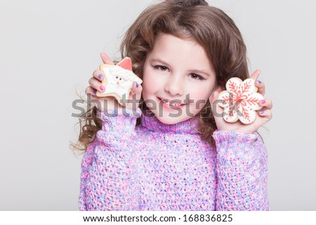 Cute child eating sweet homemade cookies and wearing winter woolen sweater, isolated. Beautiful littel girl with cookies. Happy baby girl smiling on white background in studio.