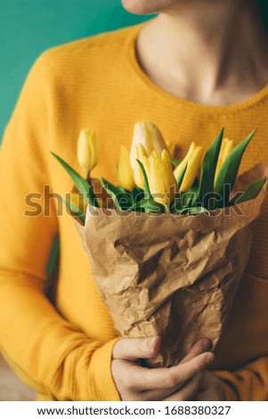 Bouquet of yellow tulips in craft paper in the hands of a woman. Blurred background