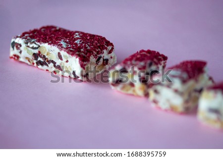 Torrone or nougat bar with nuts and red dried berries. Traditional italian dessert close up on pink background. Sweet tasty and healthy food