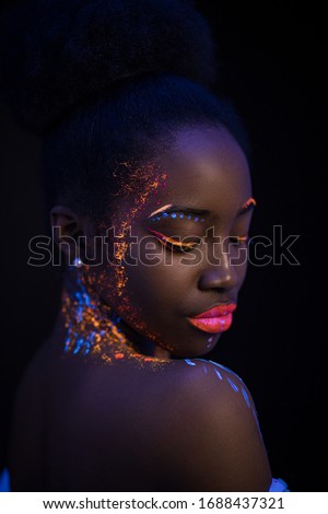 unusual portrait of beautiful african fashion woman in neon UF light. attractive young model girl with fluorescent creative psychedelic make-up, body-art