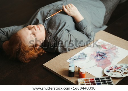Inspiration and creativity. Designer illustrator artist dreaming for new ideas laying on the floor with sketches and paints. Imagination concept