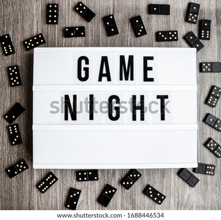 Game night text frame of dominoes with copy space inside on wooden background, table game, black Domino dice on a light wooden table, the process of playing dominoes