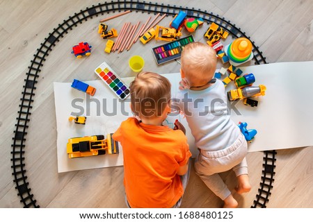 Preschool boys drawing on floor on paper, playing with educational toys - blocks, train, railroad, vehicles at home or daycare for preschool and kindergarten. Top view. Children's art and creativeness