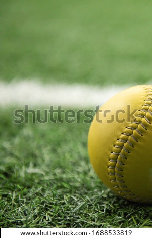 yellow softball on green synthetic astroturf grass with white painted line