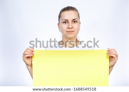 A girl in a white T-shirt is holding a yellow blank large sheet of banner.