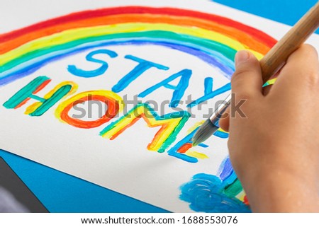 Kid painting during quarantine at home. Rainbow with words Stay at home. Social media campaign for coronavirus prevention