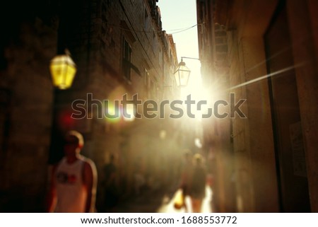 Abstract background with defocused street view at sunset with unrecognizable blurred people walking in sunset light. Modern urban life background. European old town.