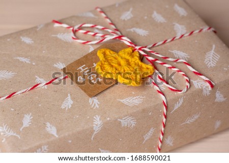 Craft homemade gift packaging with leaves print, crochet yellow star, bandaged with red and white jute rope with the inscription on the tag, gift box for the holidays