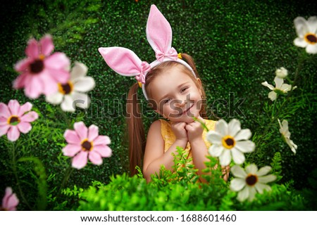 Cute smiling girl with bunny ears  is smiling surrounded by flowers and greenery. Beauty. Childhood. Spring-summer session.