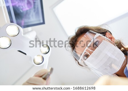 Young dentist with surgical mask and visor during a treatment or dental surgery in the dental clinic Royalty-Free Stock Photo #1688612698