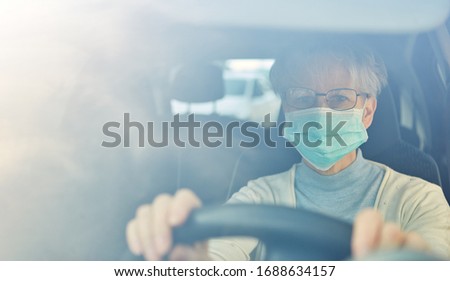 Elderly woman with a face mask driving a car as a risk group in the Covid-19 coronavirus epidemic