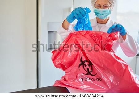 Medical cleaner with protective clothing disposes of infectious waste in a clinic during a Covid-19 coronavirus epidemic Royalty-Free Stock Photo #1688634214