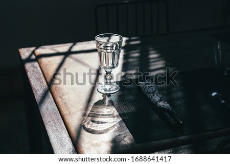 A glass goblet on a leg stands on a table among the shadows in the sunlight