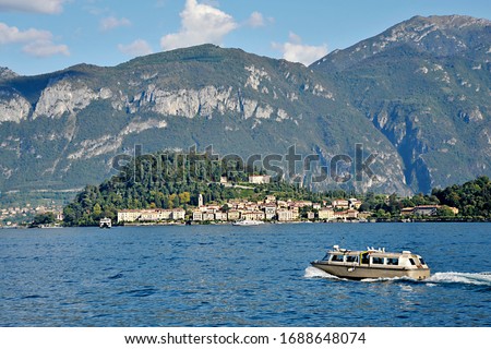 A day trippers boat is heading towards a pretty village on Lake Como, Largo di Como, surrounded by the superb pre-alpine Mountains 