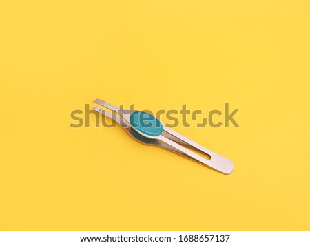Metal eyebrow tweezers, top view on yellow background