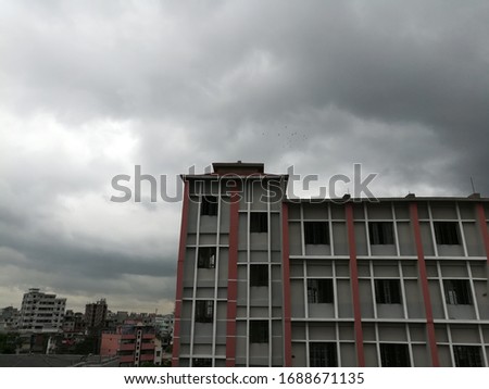 facade of a building in a cloudy day in Dhaka city in Bangladesh. The grey and maroon colored building has a vintage feel to it with clouds providing an ash colored background