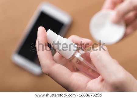 Woman hand holding antiseptic for disinfect screen of mobile phone. Female cleaning with sanitizer gel. Coronavirus or covid-19 prevention. Protection concept