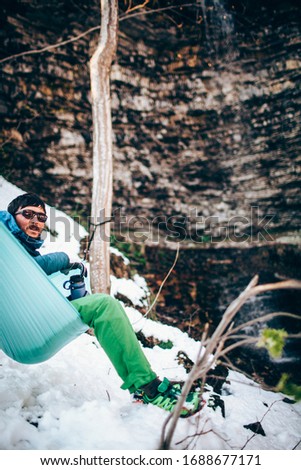 Young man sitting in a hammock on a beautiful sunny day in the in the winter forest near rock