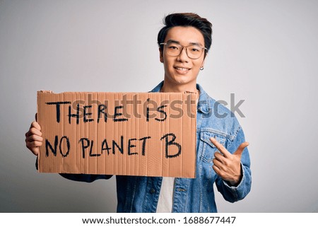 Young handsome chinese activist man protesting asking for care the planet on manifestation very happy pointing with hand and finger