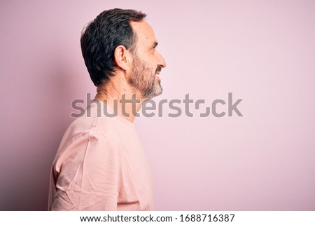 Middle age hoary man wearing casual t-shirt standing over isolated pink background looking to side, relax profile pose with natural face with confident smile.