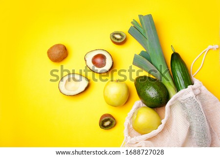 Textile string eco bag on a yellow background. Avocado, kiwi, lemon and cucumber. Flat lay style. Coronavirus concept. Delivery of products