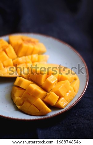 Cut mango halves on a plate. Selective focus, dark blue background.