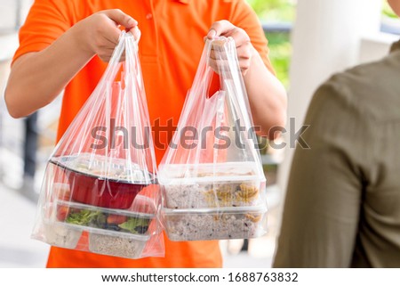 Delivery man in orange uniform delivering Asian food boxes in plastic bags to a customer at home Royalty-Free Stock Photo #1688763832