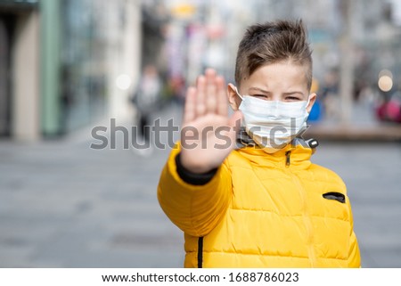 Boy in protective sterile medical mask on his face looking at camera outdoors, on  street show palm, hand, stop no sign. Air pollution, virus, Pandemic coronavirus concept.