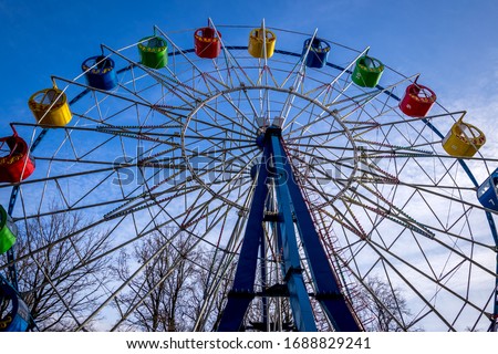 Ferris wheel with colorful cabs against the sky with clouds in the park on a sunny spring day.