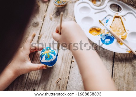 The child paints eggs for Easter. Hands of baby with brush and blue easter egg